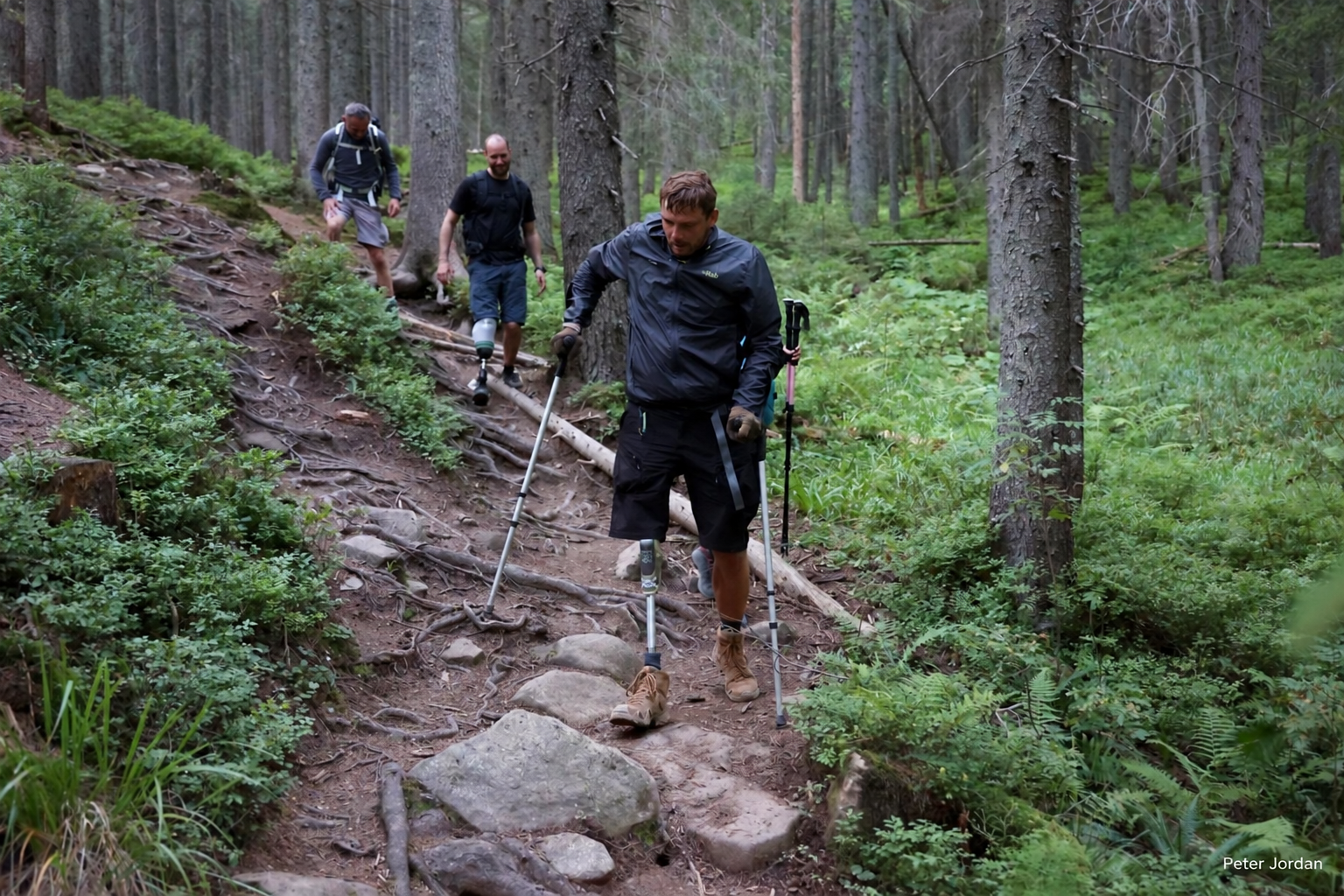Injured veterans navigating a steep, rocky trail through the Carpathian forest